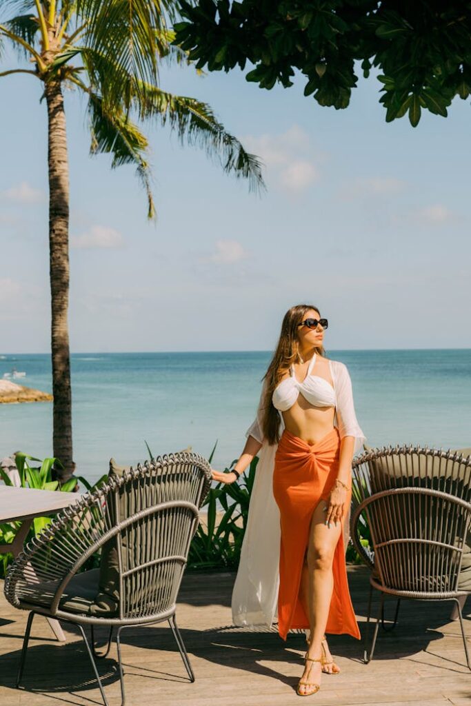 Elegant model posing by the ocean under palm trees in Bali, embracing tropical vibes.