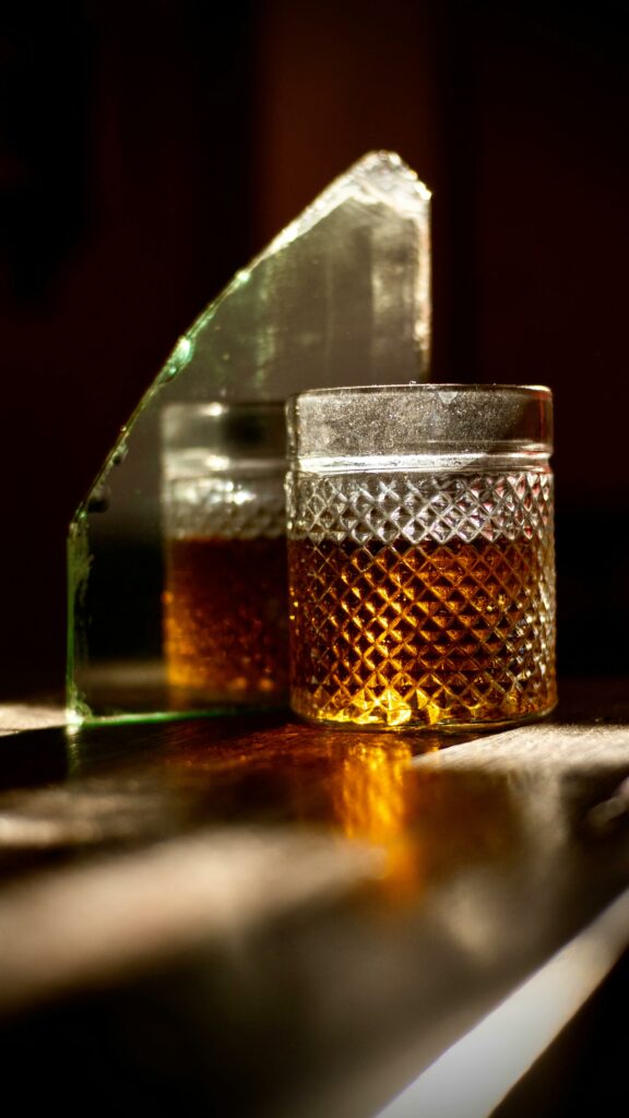 A whiskey glass sits on a reflective surface with warm lighting, capturing a luxury ambiance in Bali.